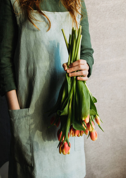 A girl in a linen dress holds a bouquet of tulips with buds down - Foto, Imagen