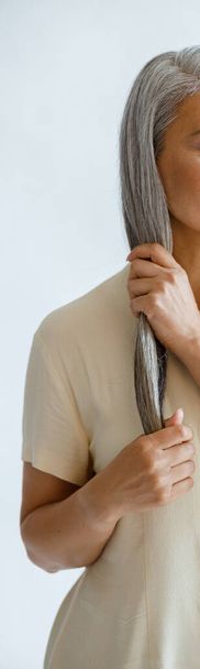 Rento keski-ikäinen aasialainen nainen pusero aivohalvauksia lukko hopea hiukset kevyellä taustalla - Valokuva, kuva