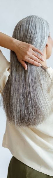 Middle aged woman adjusts long loose hoary hair on light grey background - Photo, Image