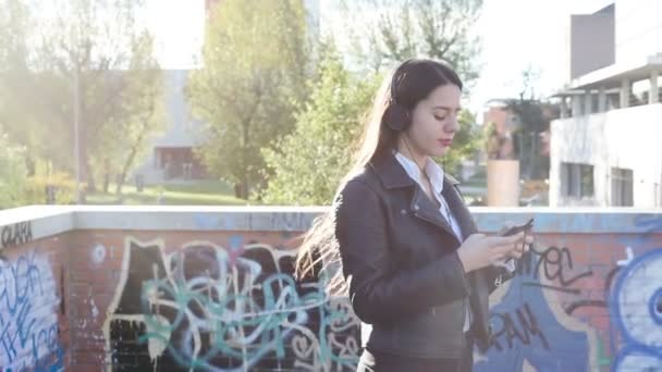 Νεαρή καυκάσια γυναίκα εξωτερική ακουστική μουσική φορώντας ακουστικά χρησιμοποιώντας smartphone surfing web - Πλάνα, βίντεο