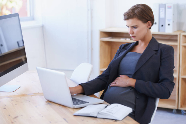 Las mujeres modernas pueden hacerlo todo. Una mujer de negocios embarazada trabajando en un portátil en su escritorio de la oficina. - Foto, imagen