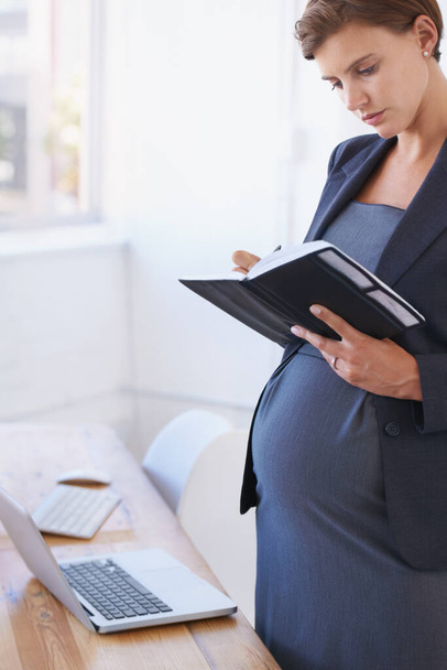 Bevestiging van haar zwangerschapsverlof. Een zwangere zakenvrouw die haar dagelijkse planner in haar kantoor leest. - Foto, afbeelding