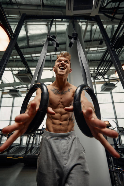 強い男がジムで体操リングに運動を行います。ライト スポーツ ホールで体操リング トレーニング フィットのオスの運動選手 - 写真・画像