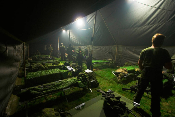 Turning in after a hard day of training. Soldiers getting ready to bunk down inside of their large tent. - Photo, Image