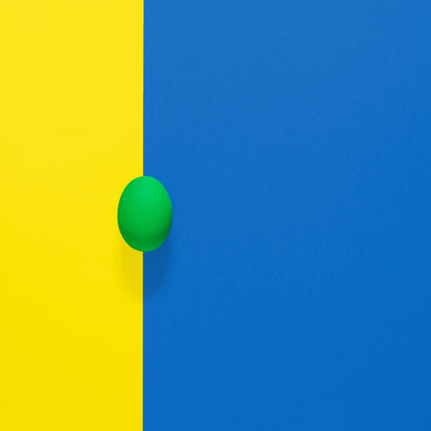 Zöld húsvéti tojás kék és sárga geometriai háttérrel. Square flat lay kompozíció másolási hellyel, minimális húsvéti ünnepi koncepció - Fotó, kép