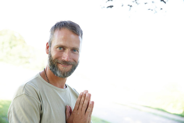 Namaste. Portret przystojnego dojrzałego mężczyzny stojącego z rękami w pozycji modlitewnej na zewnątrz. - Zdjęcie, obraz