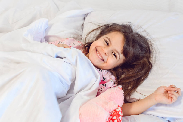 Adorable dark hair girl sleeping sweetly in the morning on wihte bed linens at home. Childrens dreams, comfort, rest and peace. 4-5 years girl. - Fotografie, Obrázek