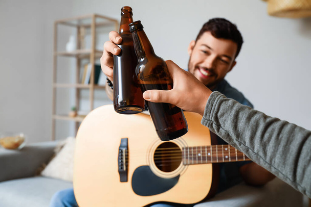 Amici maschi con bottiglie di birra e chitarra a casa - Foto, immagini