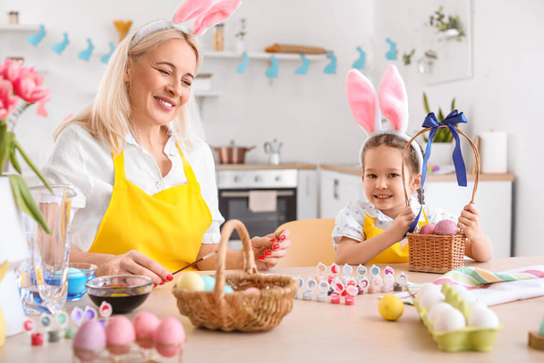 Το κοριτσάκι και η γιαγιά της βάφουν πασχαλινά αυγά στο σπίτι. - Φωτογραφία, εικόνα