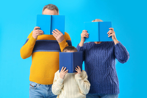 Ένα αγοράκι με τους παππούδες του με ζεστά πουλόβερ να διαβάζουν βιβλία σε μπλε φόντο. - Φωτογραφία, εικόνα