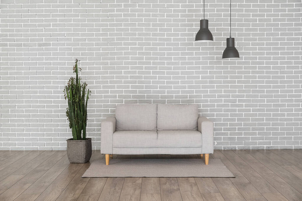 Sofá moderno e cacto perto de parede de tijolo cinza - Foto, Imagem