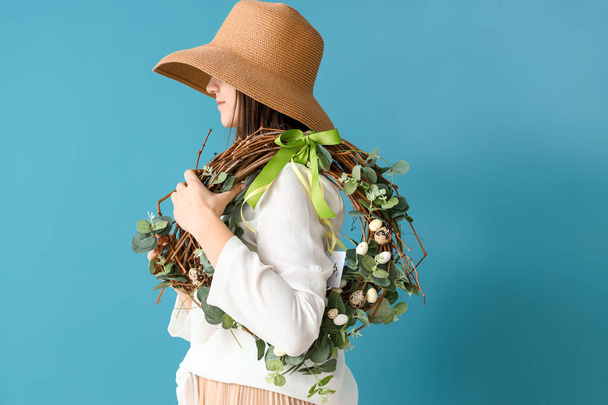 色の背景にイースターの花輪を保持スタイリッシュな帽子を持つ女性 - 写真・画像