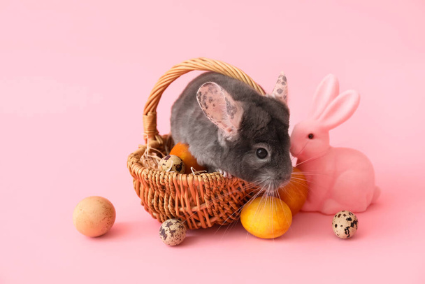 Roztomilé chinchilla v proutěném koši, hračky králíček a velikonoční vajíčka na růžovém pozadí - Fotografie, Obrázek