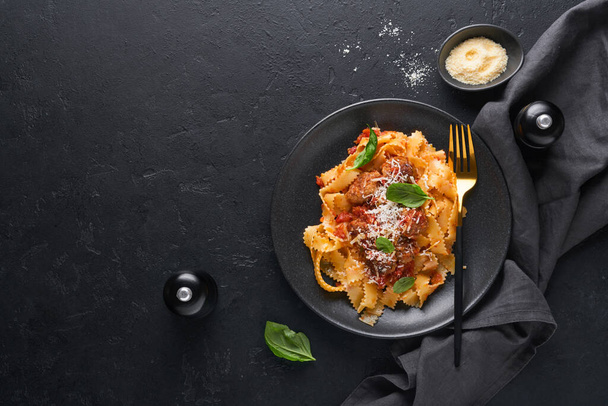Tagliatelle pasta with meatballs in tomato sauce, basil and parmesan cheese on black stone or concrete background. Traditional Italian dish and cuisine. Top view with copy space. - Valokuva, kuva