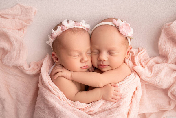Pequenas gémeas recém-nascidas. Um gémeo recém-nascido dorme ao lado da irmã. Meninas gêmeas recém-nascidas no fundo de um cobertor rosa com ligaduras rosa. As meninas gentilmente abraçar e beijar sua irmã em uma pose bonito. - Foto, Imagem