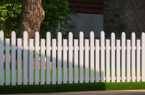 Vooraanzicht van wit houten hek op kunstgras met zonlicht en schaduw op het oppervlak in de voortuin gebied thuis - Foto, afbeelding