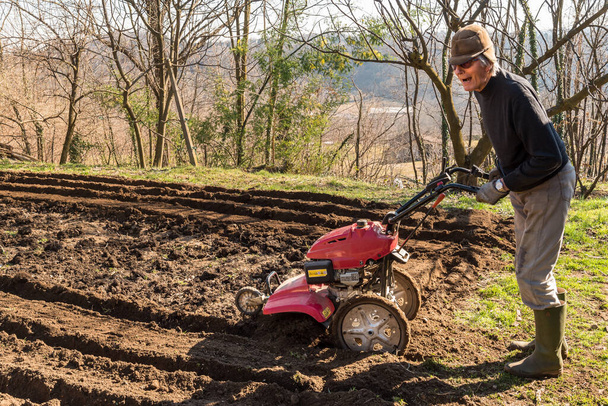 Idősebb ember talajművelést végez egy rototillerrel a kertben. Tavaszi kerti előkészítés vetésre. - Fotó, kép