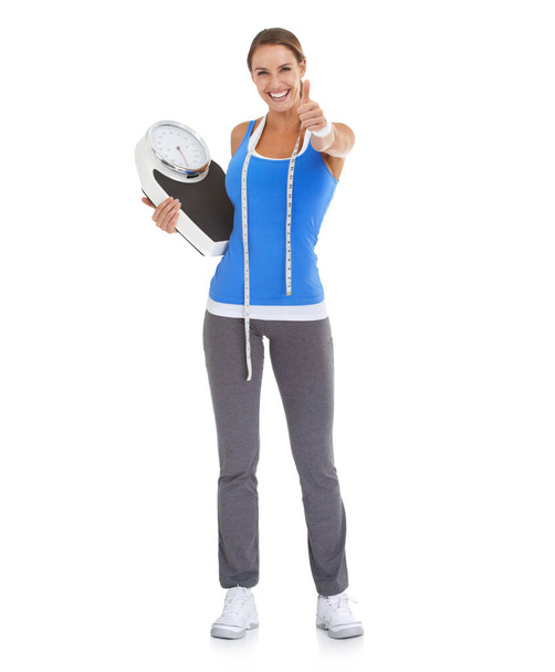 I did it, and so can you - Weight loss goals. Fit young woman giving you a thumbs up against a white background while holding a scale. - Foto, Imagen