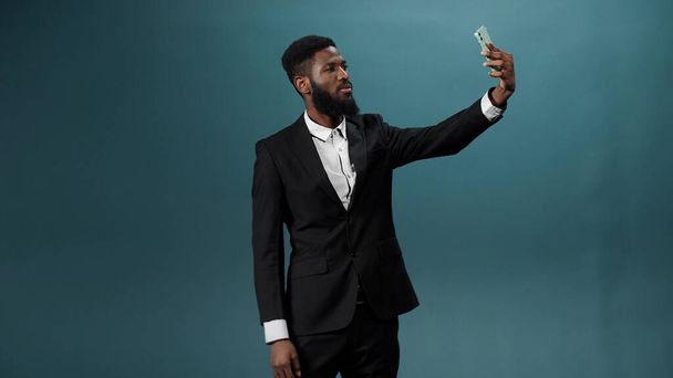 Красивый африканский мужчина с тёмной бородой в белой рубашке и чёрном костюме фотографирует на телефон. - Фото, изображение