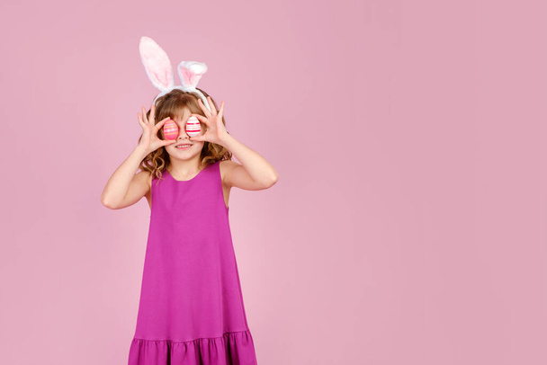 Delighted child covering eye with eggs during Easter party in pink studio - Photo, Image