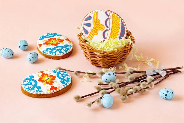 Colorido pan de jengibre pintado en forma de huevo de Pascua en la cesta y en la mesa. Las galletas de jengibre están cubiertas con glaseado de azúcar y decoradas con hermosos patrones de color. Huevos azules decorativos y ramas de sauce - Foto, imagen
