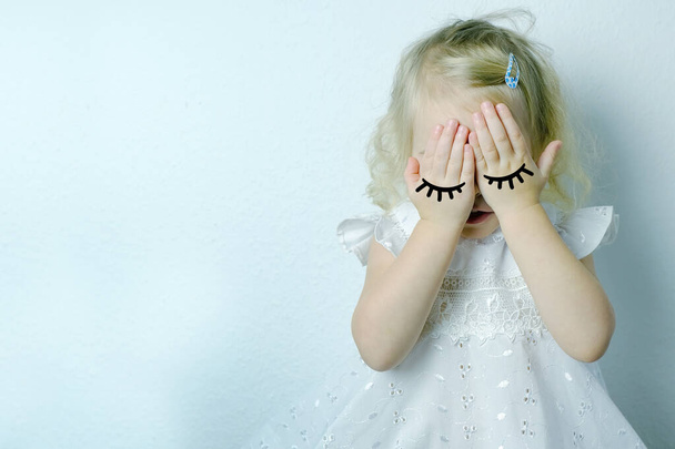 small child, blonde girl 2 years old in white dress covered her eyes with her hands from resentment, concept of children's whims, parental abuse, psychological violence, difficult childhood - Valokuva, kuva