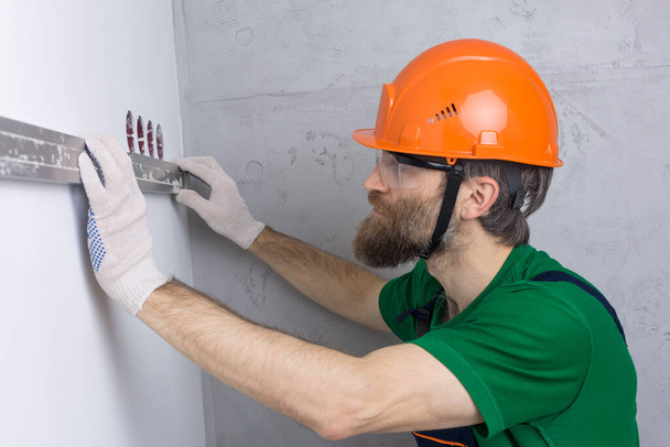Un électricien installe des prises de courant dans l'appartement. Un gars avec un casque orange et des combinaisons fait de l'électricité dans la maison. - Photo, image