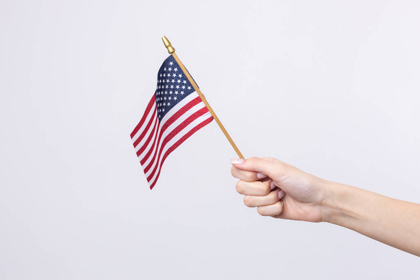 A beautiful female hand holds an American flag on a white background. - Foto, Imagen