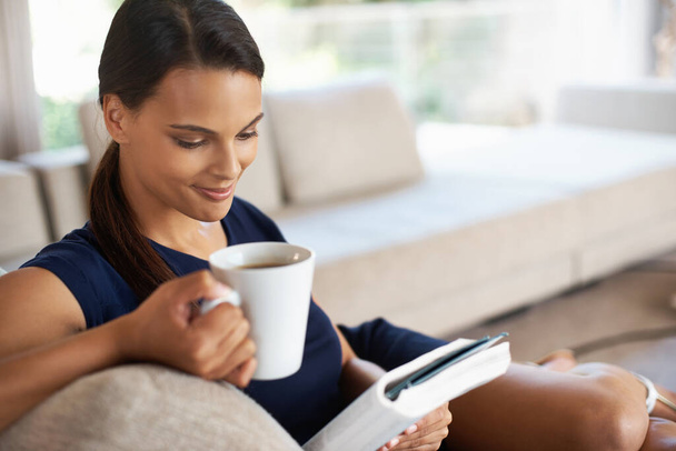 Un tiempo de relajación bien merecido. Foto de una hermosa joven relajándose con un libro y una taza de café en casa. - Foto, Imagen