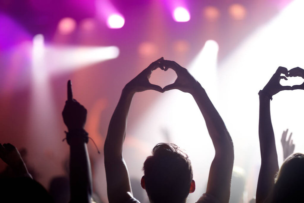 Montrer un peu d'amour pour le groupe. Vue arrière de personnes dans le public lors d'un concert de musique levant la main dans un symbole de coeur. - Photo, image