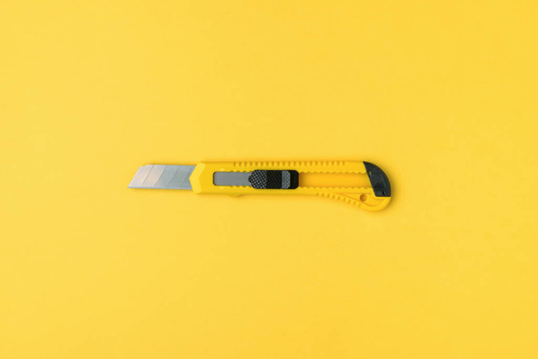 黄色の背景に黄色の文房具ナイフ。最小限のコンセプト。中心的な構成。創造性と教育のためのツール。平敷. - 写真・画像