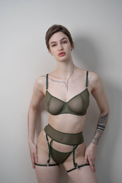 young beautiful woman posing in green lingerie in the studio, standing near a white wall - Photo, Image