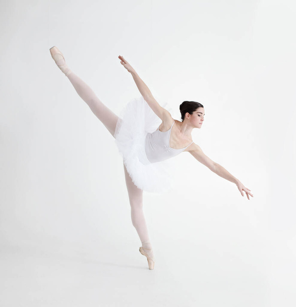 Balance is crucial. Elegant young ballerina dancing en pointe against a white background in penche position. - Fotó, kép