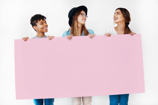 Die Damen werden diesen lieben. Studioaufnahme einer Gruppe junger Frauen mit einem leeren Plakat vor weißem Hintergrund. - Foto, Bild