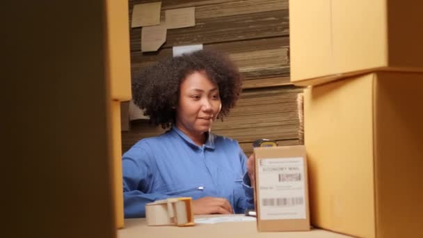 Afroamerykańska pracownica w mundurze bezpieczeństwa, używająca skanera kodów kreskowych do sprawdzania zamówień wysyłkowych w magazynie paczek, fabryka produkcji papieru dla przemysłu opakowaniowego, logistyczna obsługa transportowa. - Materiał filmowy, wideo