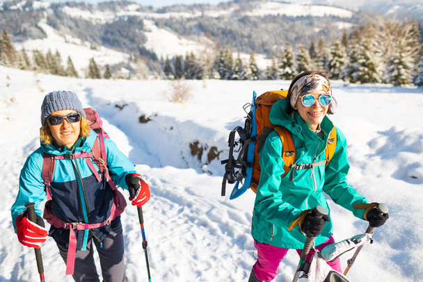 Two women walk with snowshoes on the backpacks, winter trekking, two people in the mountains in winter, hiking equipment - Photo, Image