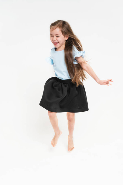 Ein Mädchen in blauem T-Shirt und schwarzem Rock. Eine kleine Schülerin mit langen Haaren. Das Mädchen tanzt und jubelt. - Foto, Bild