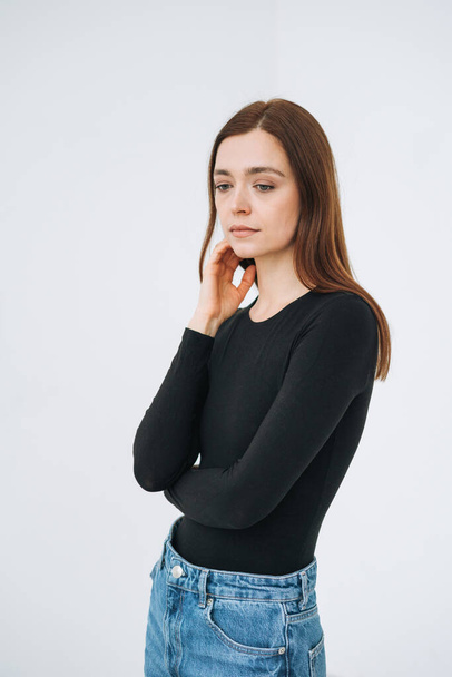 Vertical portrait of thinking young beautiful woman with dark long hair in black longsleeve and jeans in full length on white background isolated - Φωτογραφία, εικόνα