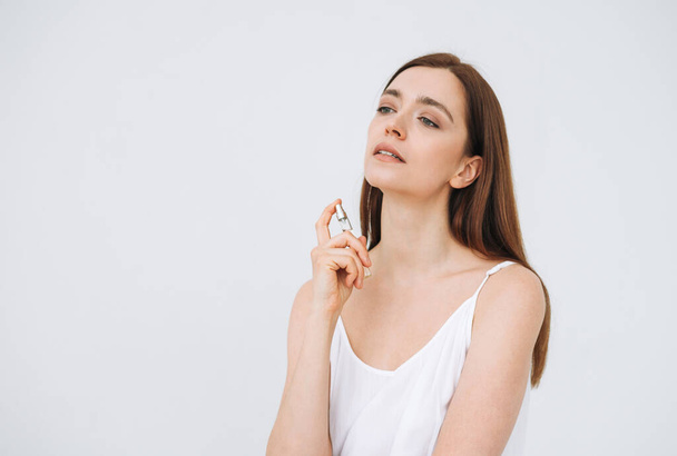 Beauty portrait of happy smiling woman with dark long hair with perfume on clean fresh skin face and hands on the white background isolated - 写真・画像