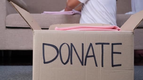 Giovane donna che mette i vestiti nella scatola delle donazioni a casa per aiutare i poveri. Concetto di donazione. - Filmati, video