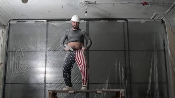 Koruyucu kasklı şişman sakallı yetişkin bir adam ve pantolonun üzerindeki Amerikan bayrağı izleri inşaat beyazlatıcısının yüksek tavanını kaldırıyor. Tamiratı kendi el konseptinle yap. 4k ağır çekim görüntüleri - Video, Çekim