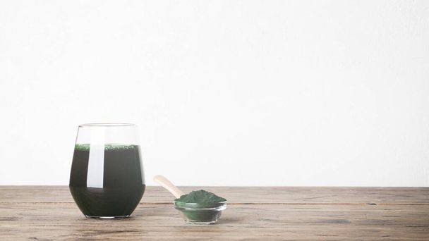 fresh green drink with spirulina in glass, spirulina powder with spoon on wooden background. useful habits - Φωτογραφία, εικόνα