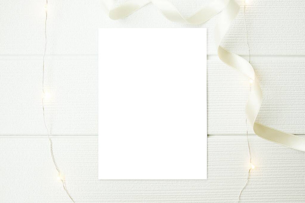 Blank greeting card mockup with cream white ribbon and light on white wood table. Top view, flatlay, white copy space. Simple and minimalistic concept. - Fotoğraf, Görsel