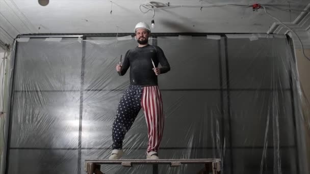 Koruyucu kasklı şişman sakallı yetişkin bir adam ve pantolonun üzerindeki Amerikan bayrağı izleri inşaat beyazlatıcısının yüksek tavanını kaldırıyor. Tamiratı kendi el konseptinle yap. 4k ağır çekim görüntüleri  - Video, Çekim