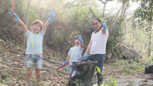 Gelukkige moeder en kind vrijwilliger geven duimen op na het oprapen van afval bij de rivier. Gooi afval in de vuilnisbak om het milieu te helpen redden. Wereldmilieudag - Video