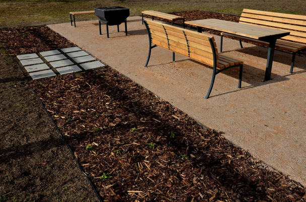 Pergola, κήπο περίπτερο είναι εξοπλισμένο με μια μεταλλική σχάρα. δημόσια ψησταριά στο πάρκο. ξύλινα τραπέζια κατασκήνωσης. γκαζόν γύρω από το μπεζ χαλίκι ανάπαυσης περιοχή στο πάρκο, νέα, άνοιξη, μαύρο - Φωτογραφία, εικόνα