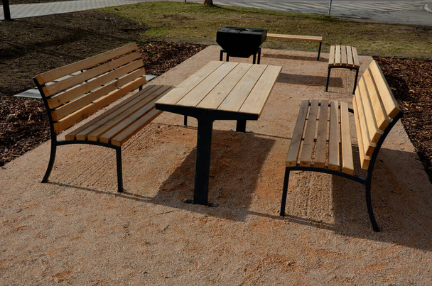 Pergola, puutarhapaviljonki on varustettu metalligrillillä. yleinen grillipaikka puistossa. puutelttapöydät. nurmikko puiston beigen soran ympärillä, uusi, kevät, musta - Valokuva, kuva