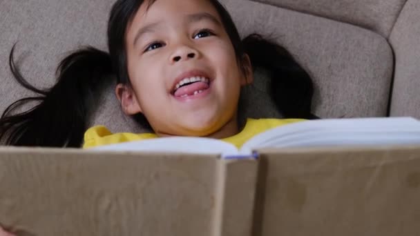 Nettes kleines Mädchen liest ein Buch, während es zu Hause auf dem Sofa sitzt. - Filmmaterial, Video