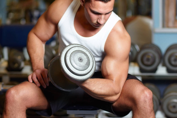 Building his biceps. A muscular young man working out in the gym. - 写真・画像