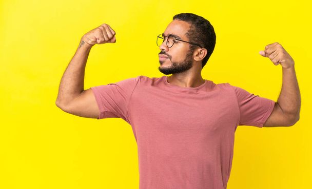 Young latin man isolated on yellow background doing strong gesture - Foto, Imagen